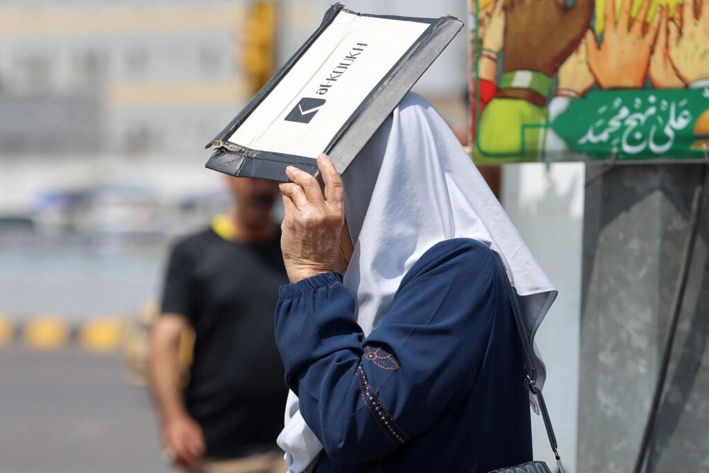 امرأة تحتمي من أشعة الشمس باستخدام ملف ورقي أثناء سيرها في شارع الجمهورية وسط بغداد، في 27 تموز 2025، خلال موجة حر شديدة. تصوير: أحمد الربيعي / وكالة فرانس برس.